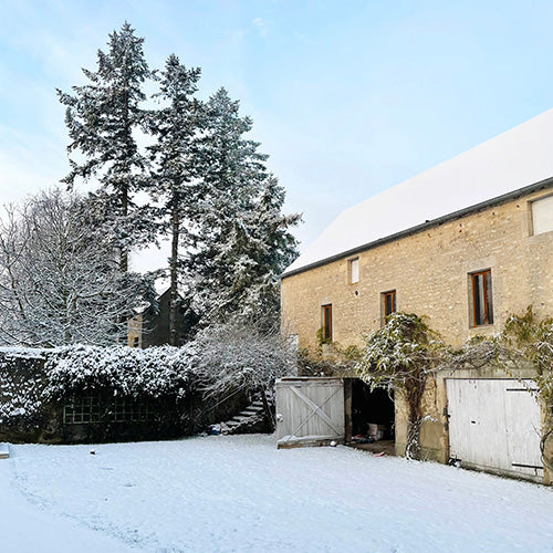 Grange normande en pierre avec une pelouse recouverte de neige